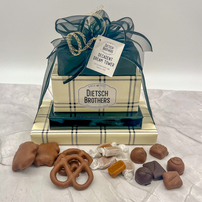 Four layered tower of assorted treats wrapped in plaid cream and black paper and solid black wrapping paper and tied with a black bow.