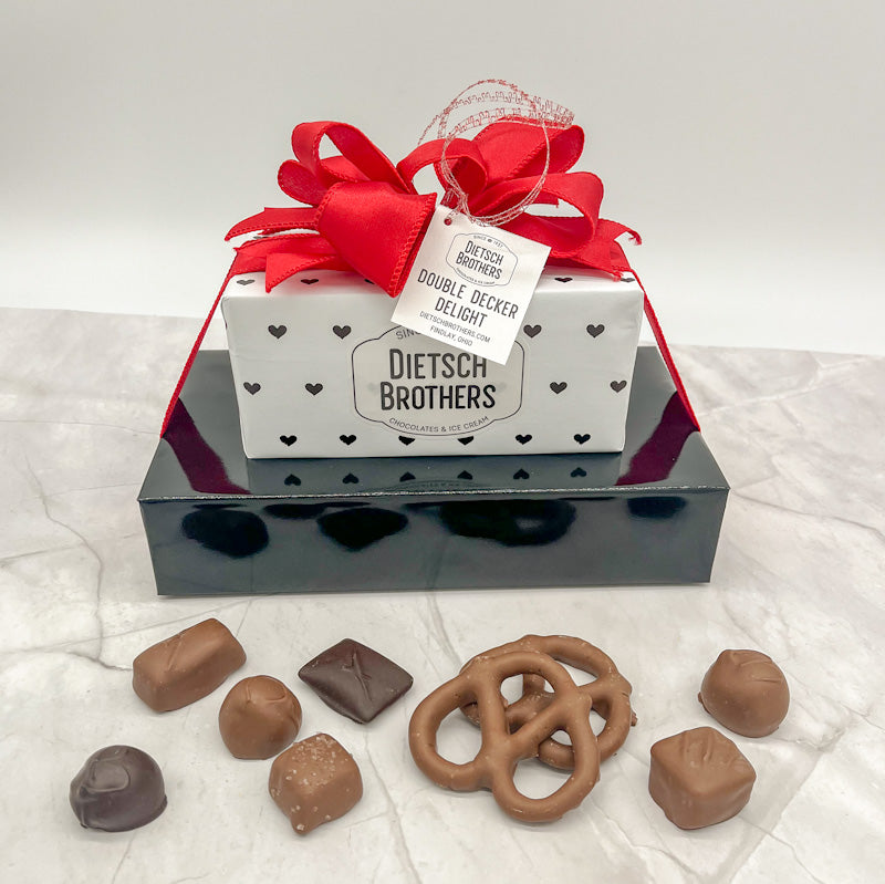 Two layered tower featuring an assortment of treats wrapped in solid black paper and white paper with black hearts, topped with a red bow