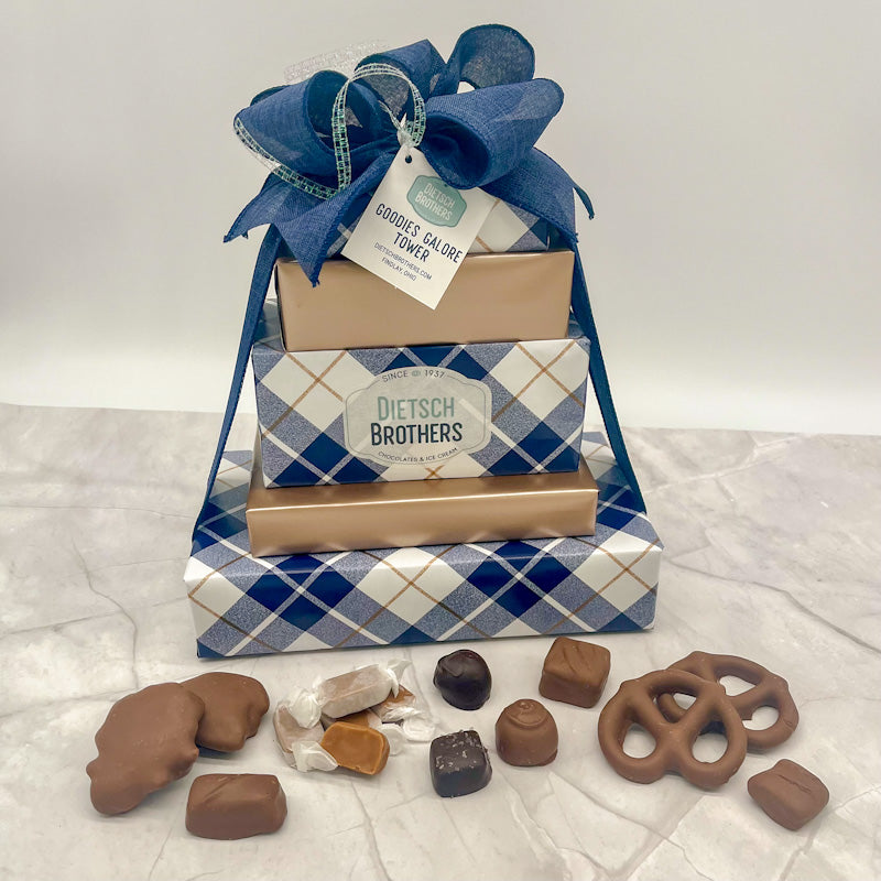 Five layered tower of assorted treats wrapped in blue plaid and gold wrapping papers and tied with a blue bow.