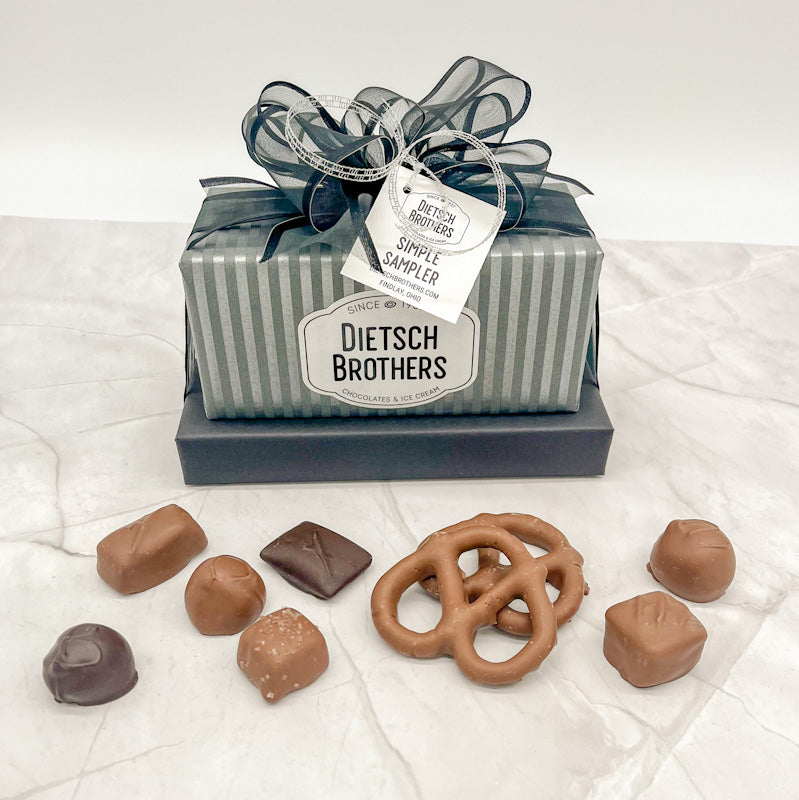 Two layered tower of assorted treats wrapped in striped silver and grey paper and solid dark navy blue paper and topped with a dark navy blue bow.