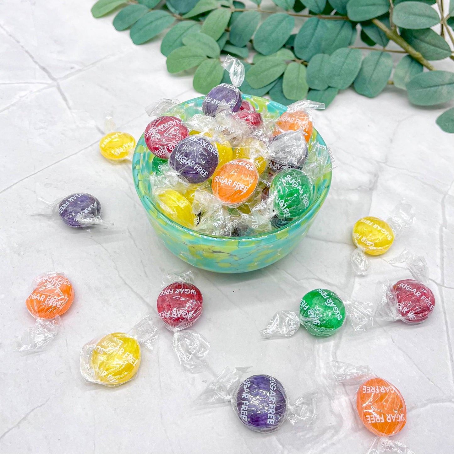 Colorful wrapped sugar free fruit candies with visible text on a light surface with green leaves.