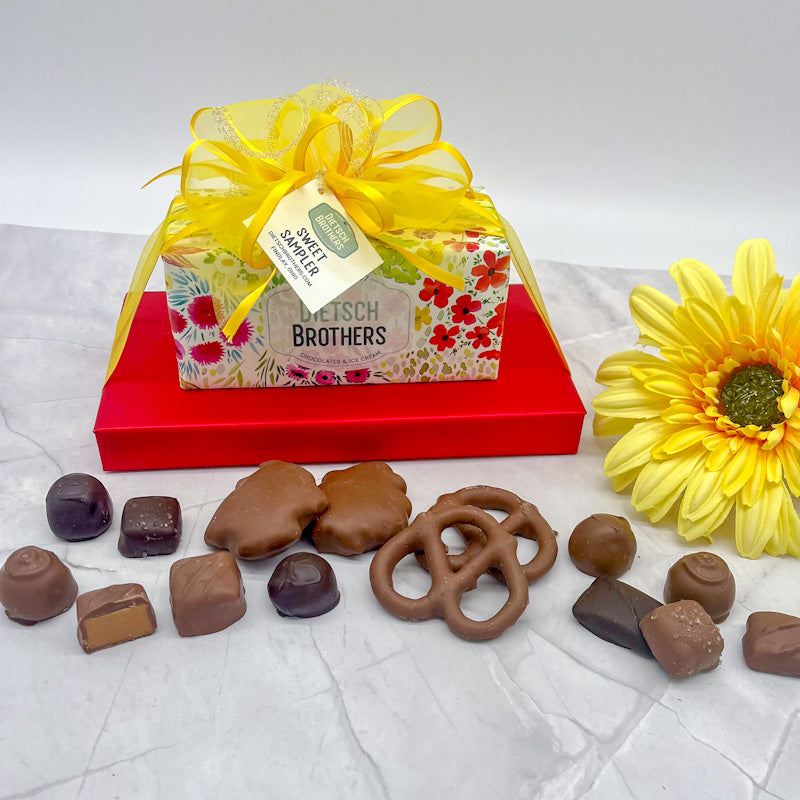 Two layered tower of assorted treats wrapped in colorful floral paper and solid red wrapping paper and topped with a yellow bow.