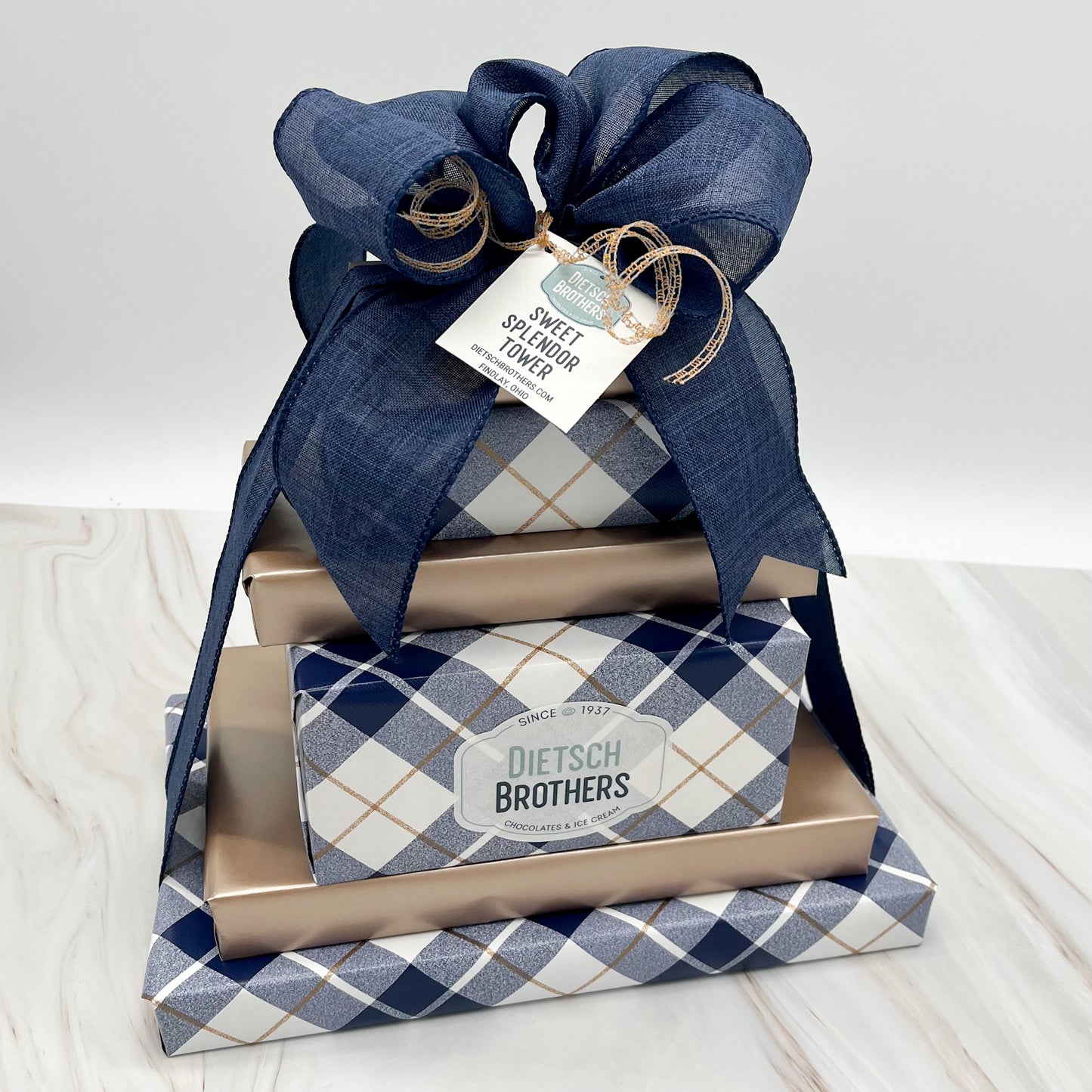Six layered tower of assorted treats wrapped in navy and white plaid paper and solid light copper wrapping paper and tied with a navy blue bow.