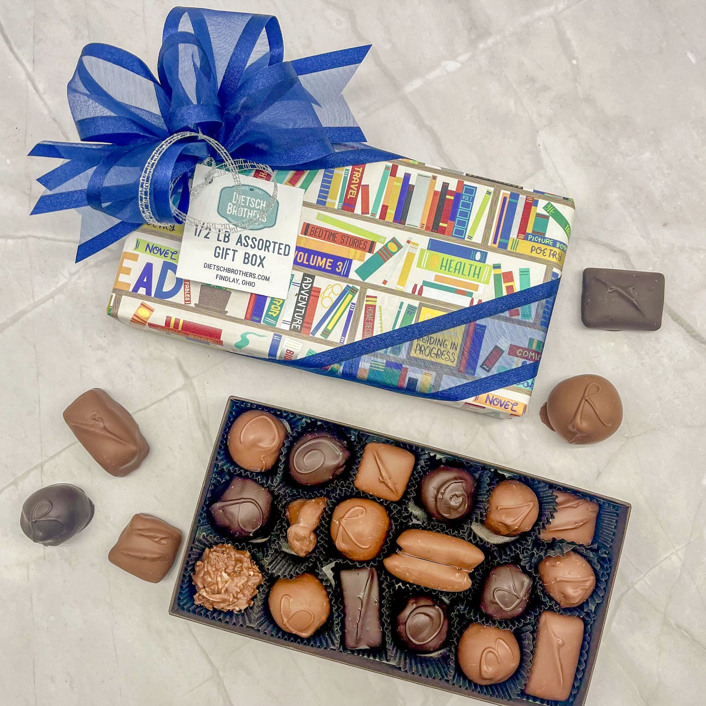 Assorted box wrapped in a teacher book shelf themed paper and topped with a blue bow