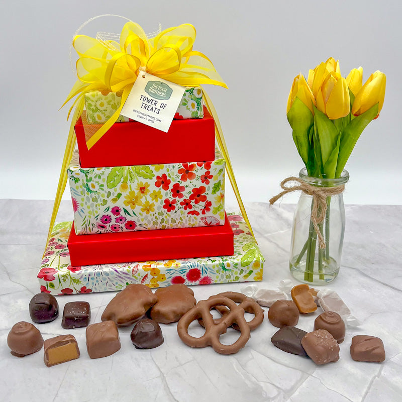 Five layered tower of assorted treats wrapped in colorful floral paper and solid red wrapping paper and tied with a yellow bow.