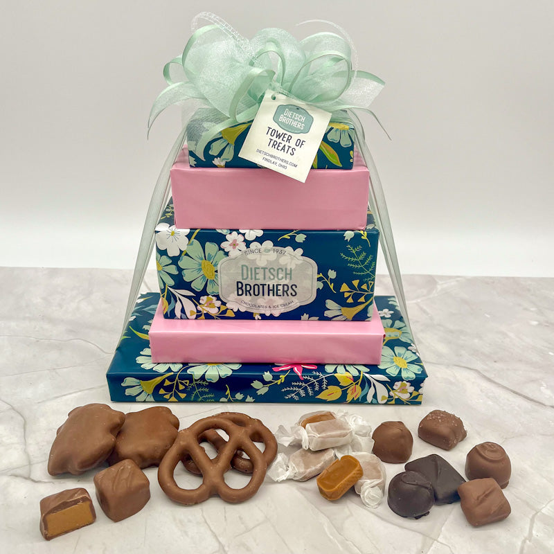 Five layered tower of assorted treats wrapped in blue floral paper and solid pink wrapping paper and topped with a mint green bow.