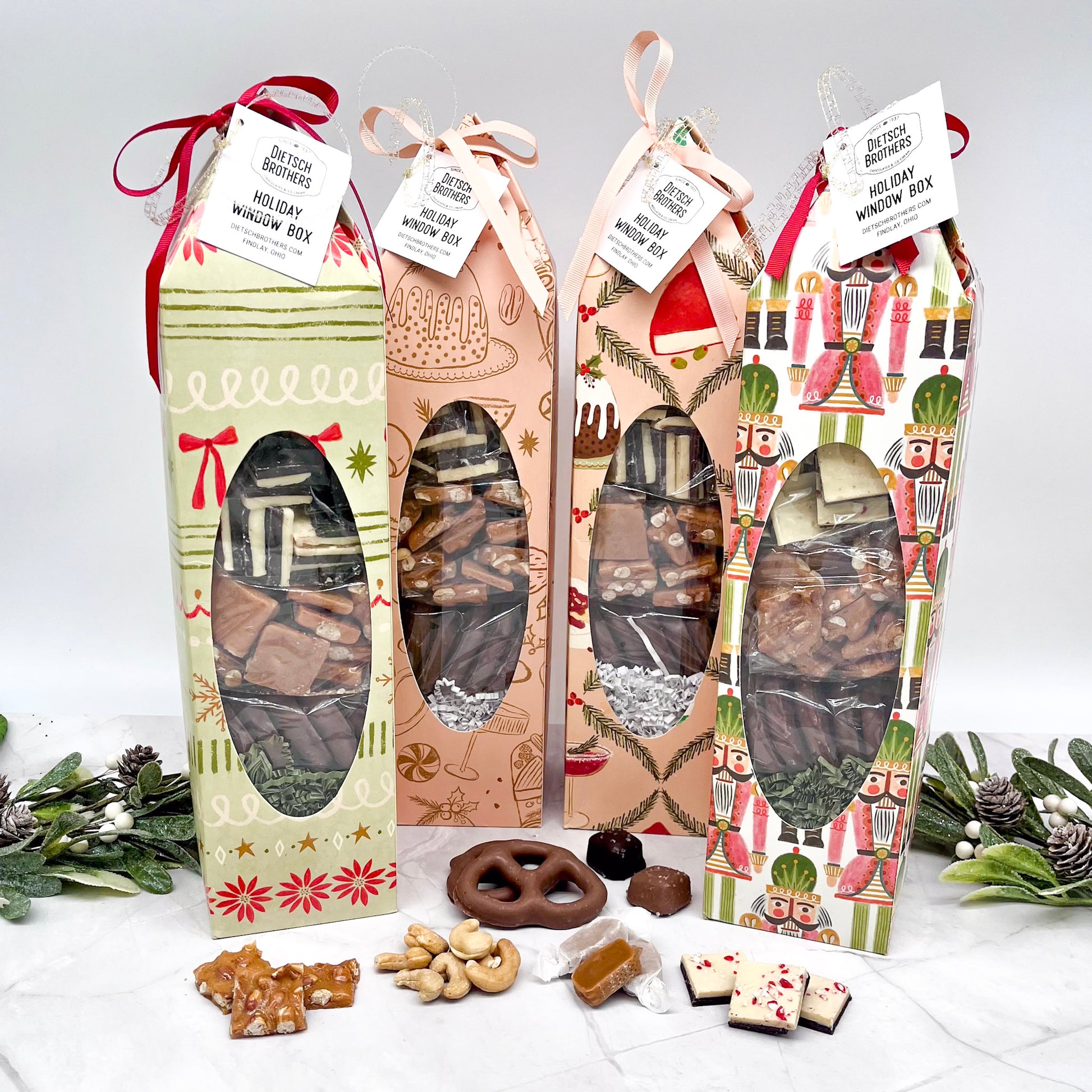Four holiday-themed gift boxes with visible chocolates and nuts on a white surface.