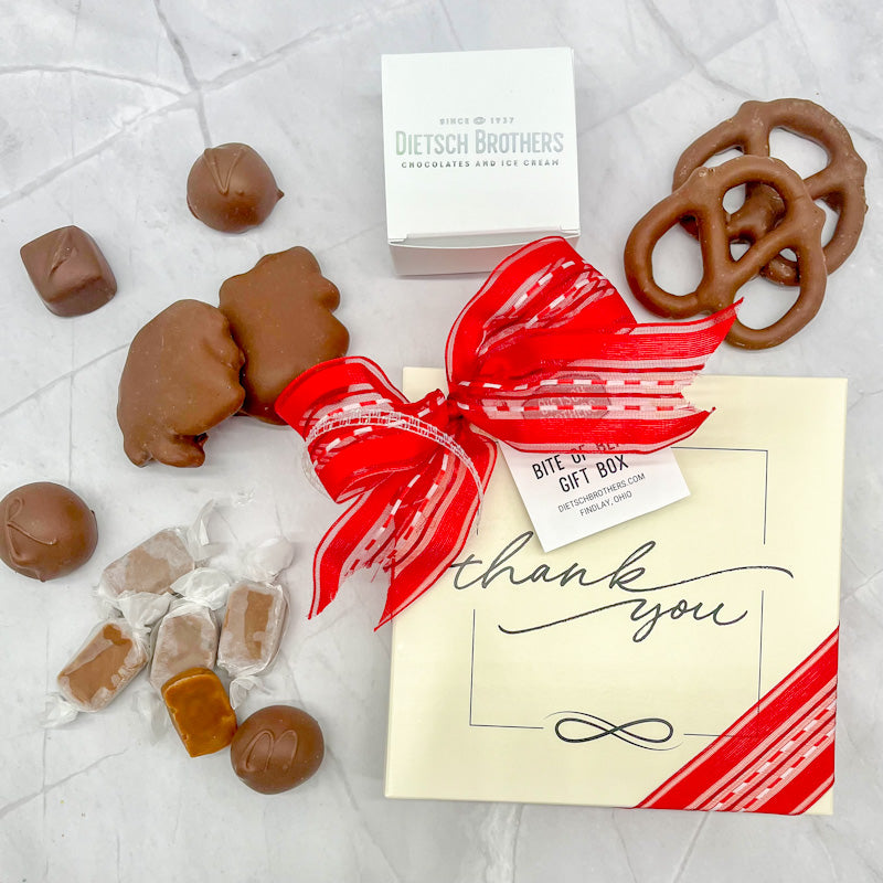 Assorted treat box featuring a cream colored box with text "thank you" across it and topped with a red bow.