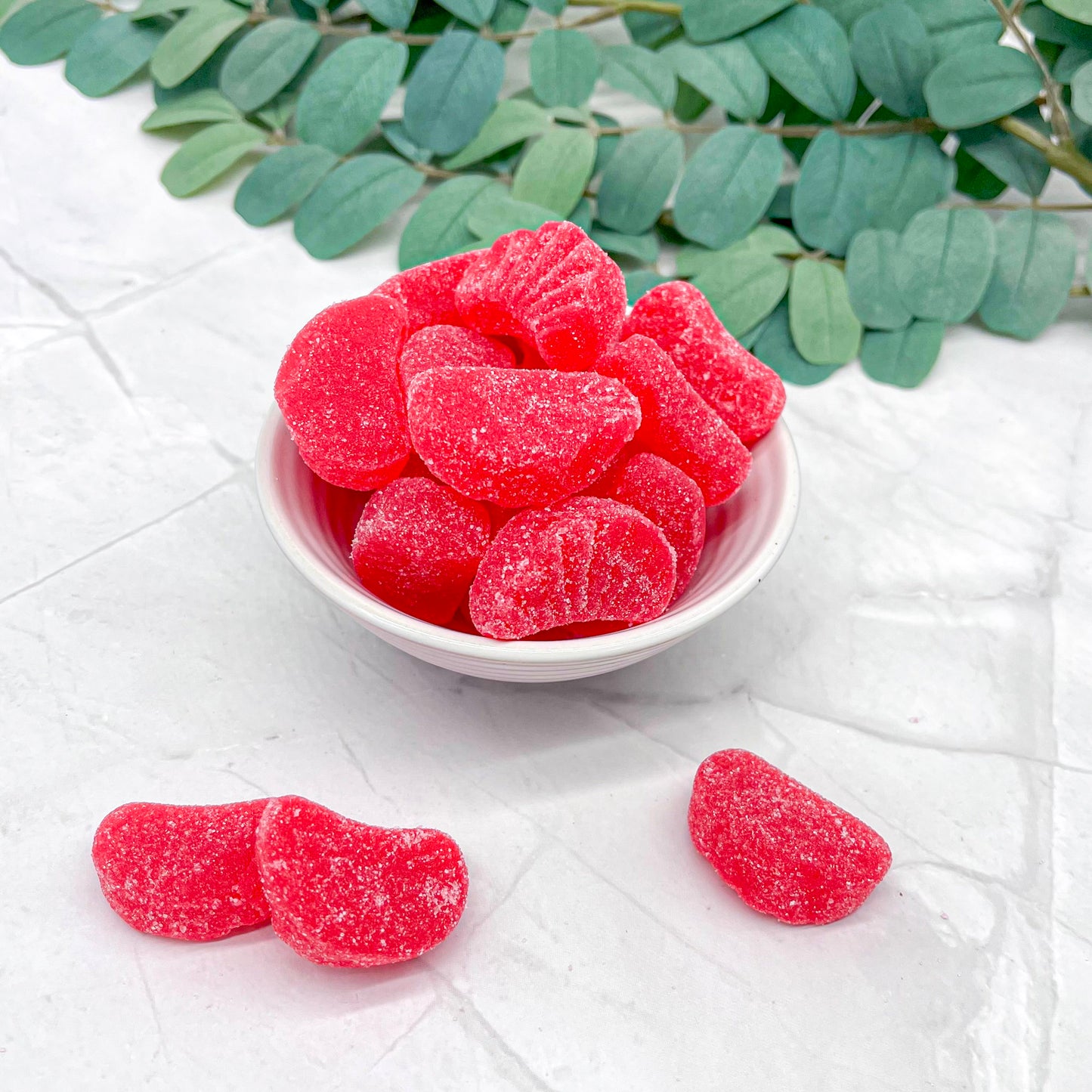 Red cherry slices in a white bowl on a light surface with green leaves in the background