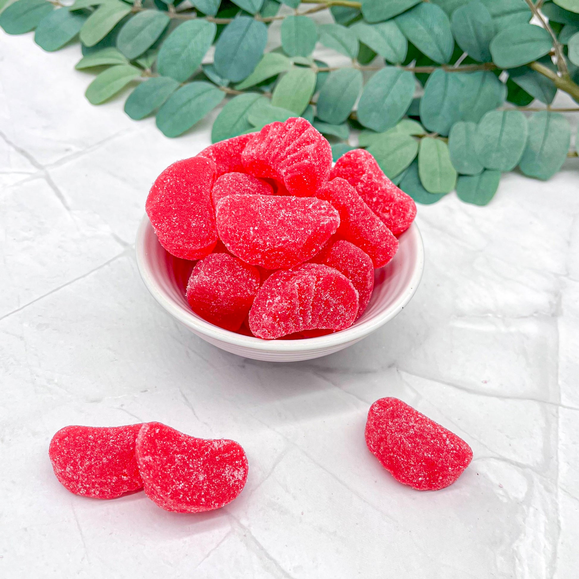 Red cherry slices in a white bowl on a light surface with green leaves in the background