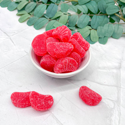 Red cherry slices in a white bowl on a light surface with green leaves in the background