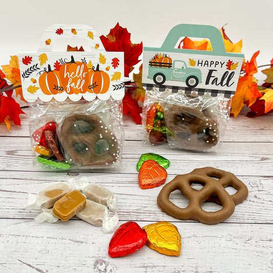 Two packages of chocolate pretzels with foil wrapped chocolate leaves and caramels on a wooden surface.