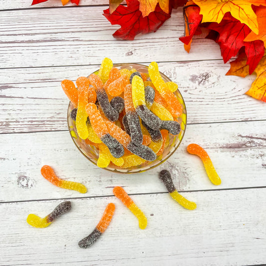 Gummy worms in a glass bowl on a wooden surface with autumn leaves.