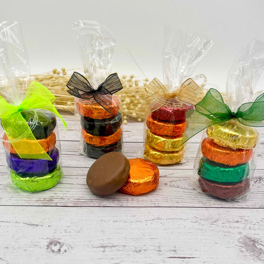Assorted colorfully wrapped chocolate covered Oreos in clear packaging with decorative ribbons on a wooden surface.