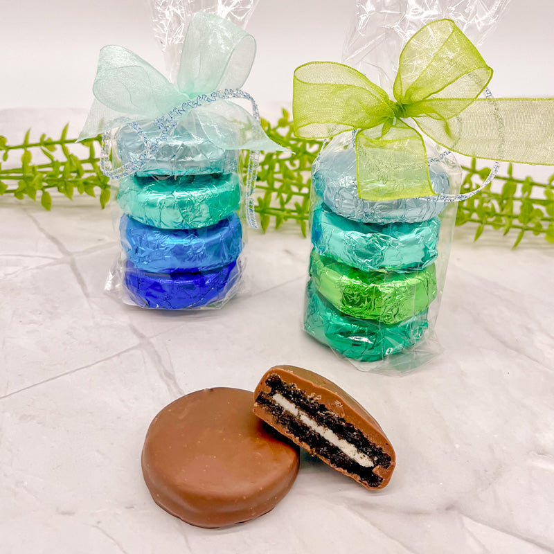 Four foil wrapped oreos featuring different shades of blue and green as well as silver foil wrap, and topped with blue or green bows. 