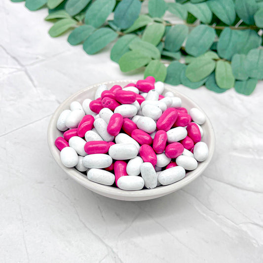 White bowl filled with pink and white candies on a light gray surface with green leaves in the background