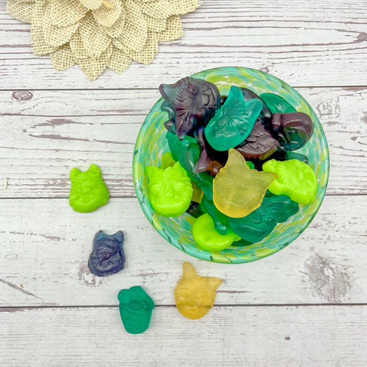 Colorful monster face-shaped candies in a glass bowl on a wooden surface with a decorative flower.