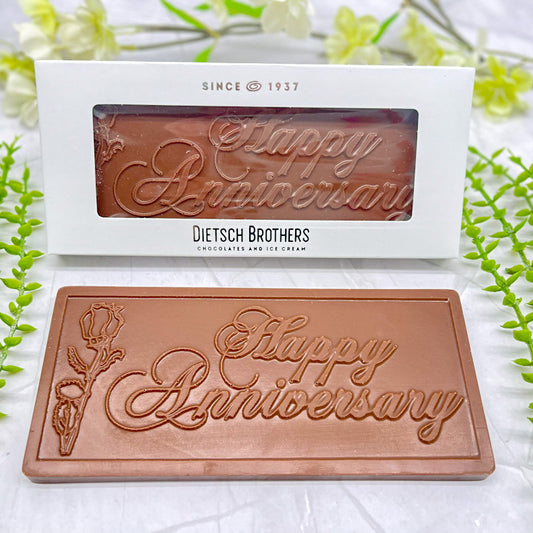 Milk chocolate bar that features a raised text "Happy Anniversary" across it, and a raised floral design to the left of the text.