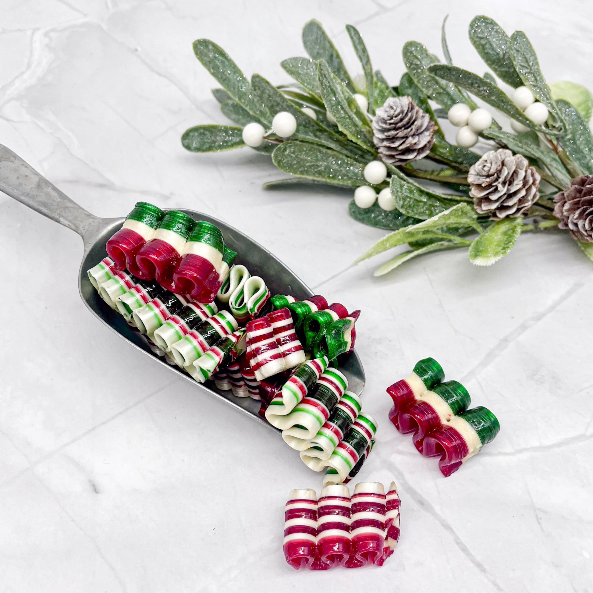 Decorative ribbon candy on a white surface with mistletoe and pine cones.