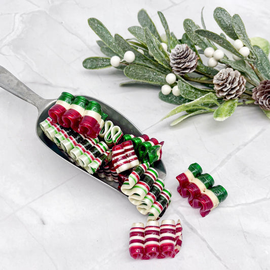 Decorative ribbon candy on a white surface with mistletoe and pine cones.