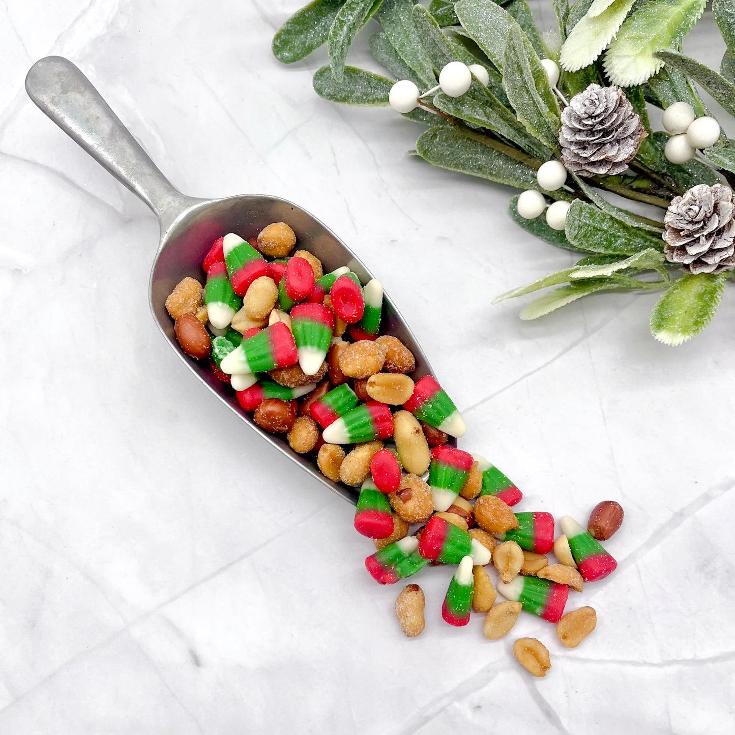Metal scoop filled with colorful candy on a white surface with decorative elements.