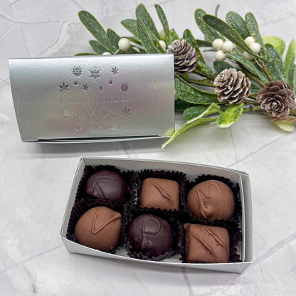 Box of chocolates with a decorative silver cover on a textured surface with greenery.
