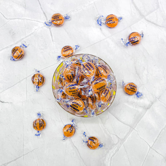 Glass bowl filled with sugar free wrapped butterscotch candies on a white marble surface