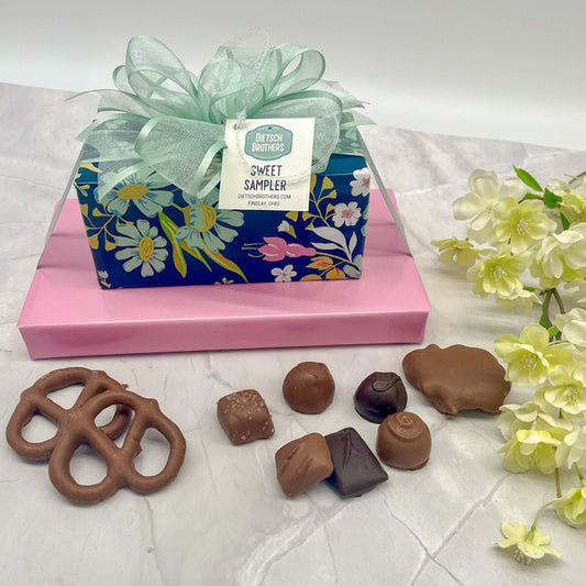 Two layered tower of assorted treats wrapped in blue floral paper and solid pink wrapping paper and topped with a mint green bow.