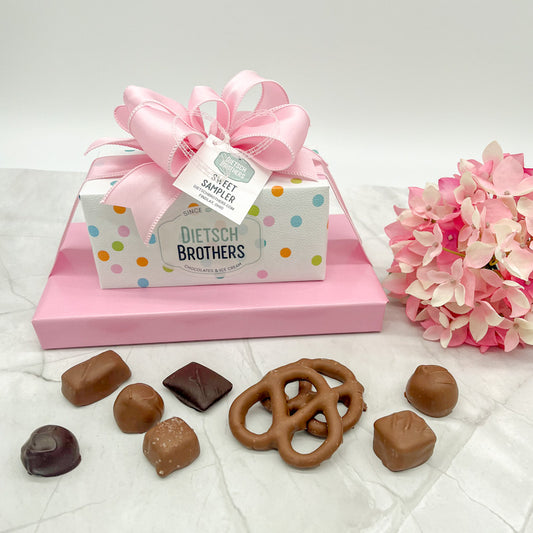 Two layered tower of assorted treats wrapped in white paper featuring multi colored dots and solid light pink paper and topped with a light pink bow.