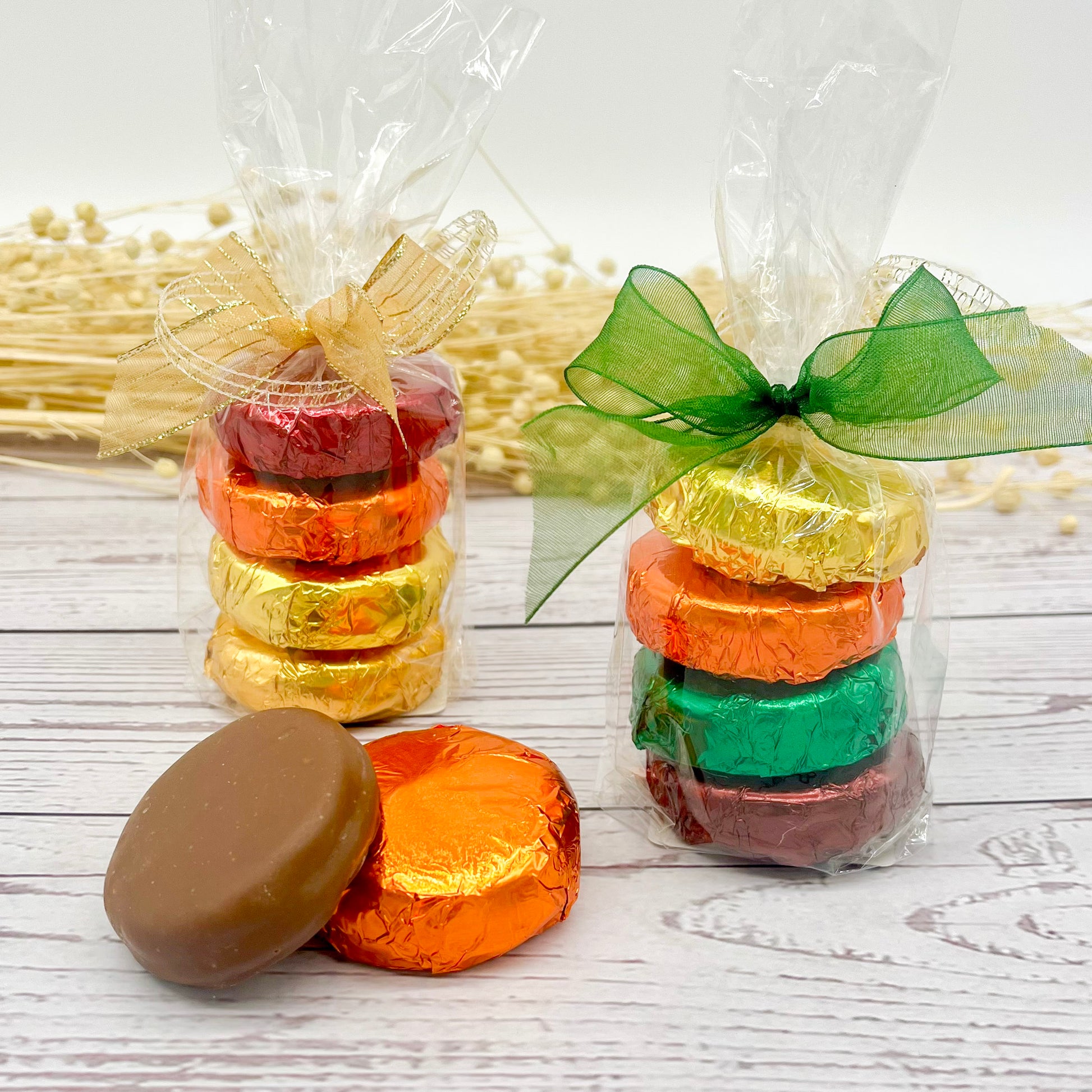 Colorfully wrapped chocolate covered Oreos in clear packaging with decorative ribbons on a wooden surface.