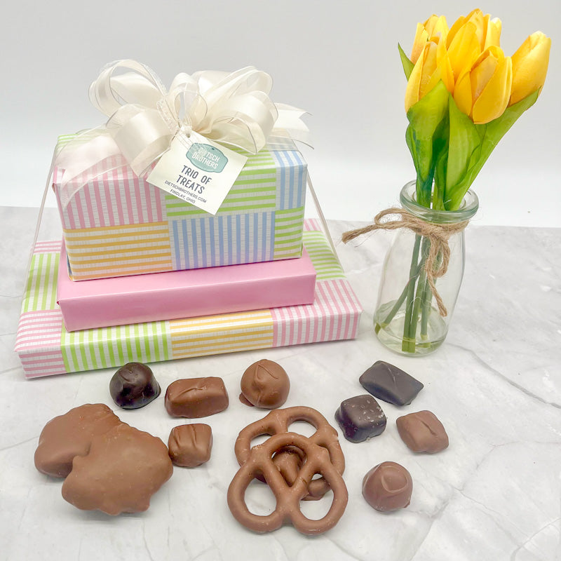 Three layered tower of assorted treats wrapped in pastel striped paper and solid light pink wrapping paper and tied with a white bow.